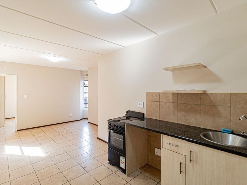 Open-plan living area featuring tiled flooring and a compact kitchen with granite countertops, built-in cabinetry, and a freestanding stove.