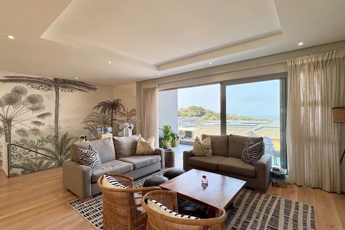 Spacious living room featuring hardwood flooring, a recessed ceiling with integrated lighting, and large sliding glass doors opening to an outdoor area with views.