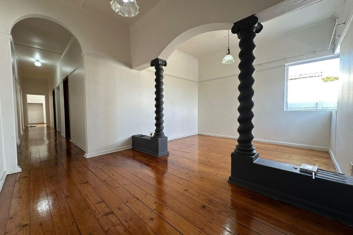 Spacious living area featuring polished timber flooring, decorative architectural columns, and an arched entryway leading to a hallway.