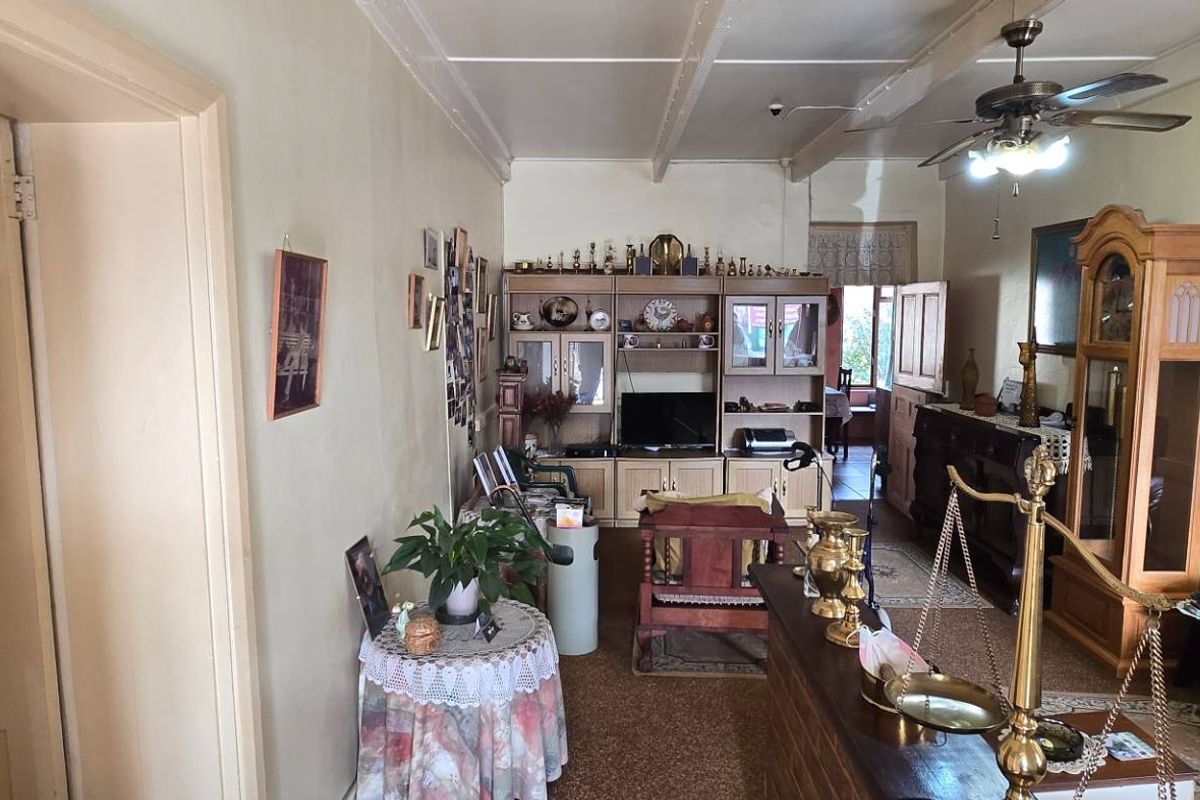 A traditional living room featuring exposed ceiling beams, a ceiling fan, and carpeted flooring, offering a dated interior space with potential for modernization.