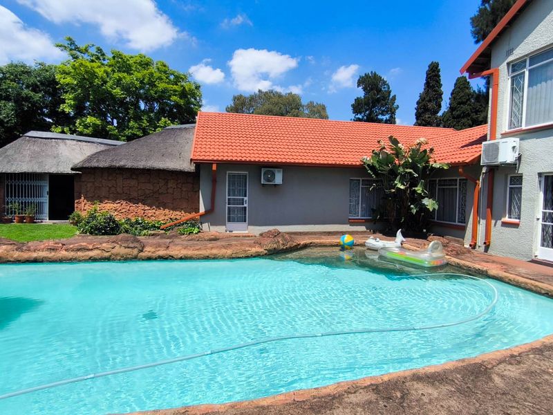 Outdoor pool area featuring a rock-edged swimming pool, adjacent thatched structure, and main house exterior with tiled roofing and security features.