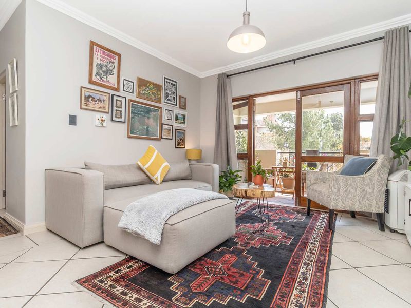 A bright and well-maintained living room featuring tiled floors, crown molding, and large sliding glass doors that open onto a private balcony.