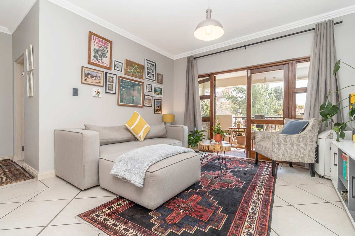 A bright and well-maintained living room featuring tiled floors, crown molding, and large sliding glass doors that open onto a private balcony.