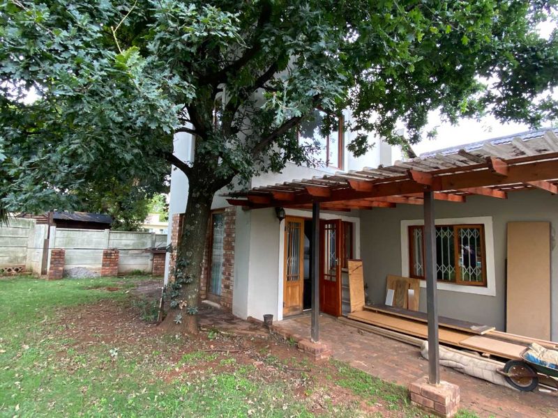 Rear exterior view of the cottage featuring a timber pergola, brick paved patio area, and mature tree in the garden.