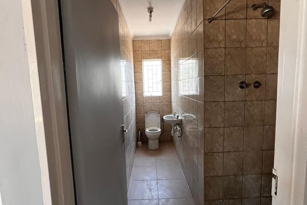 A narrow, dated bathroom featuring a walk-in shower area, wall-mounted basin, and toilet with full-height ceramic wall tiling.