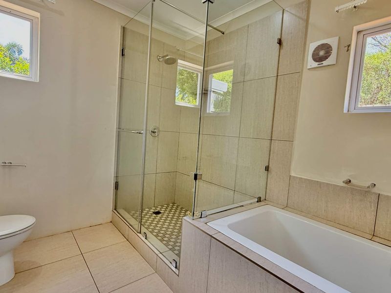 A clean and modern bathroom featuring a glass-enclosed shower, a built-in bathtub, and neutral floor-to-ceiling tiling.