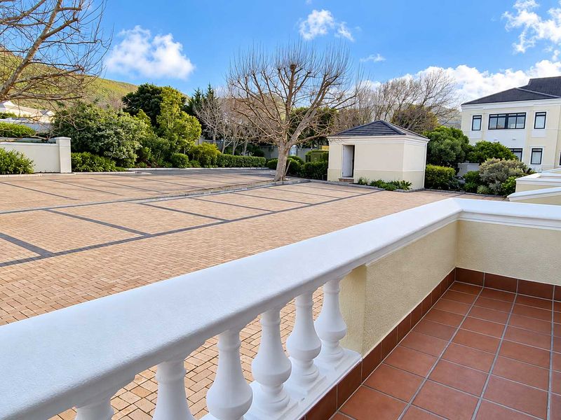 A well-maintained balcony with a classic balustrade overlooking a paved parking area and landscaped grounds.