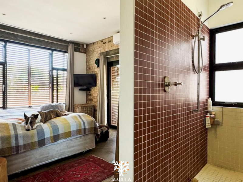 A bedroom featuring an open-plan design with an integrated shower area, exposed brick wall, and modern tiled finishes.
