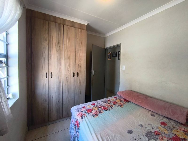 A bedroom featuring tiled flooring, a built-in wooden wardrobe, and neutral wall finishes.