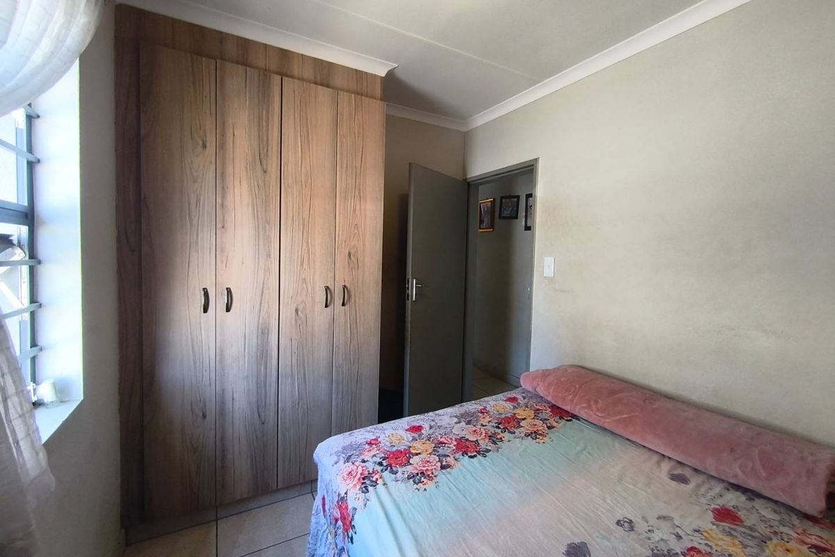 A bedroom featuring tiled flooring, a built-in wooden wardrobe, and neutral wall finishes.