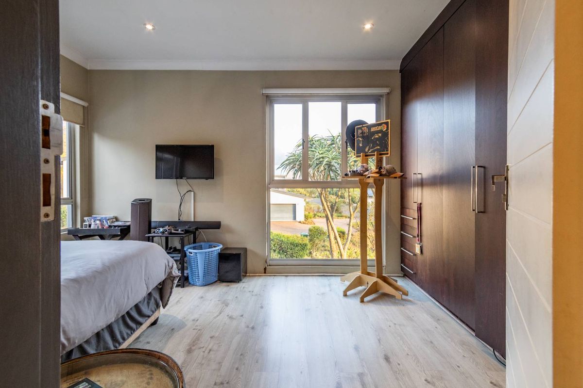 A well-lit bedroom featuring modern laminate flooring, built-in dark wood cupboards, and large windows providing natural light and a view of the exterior.