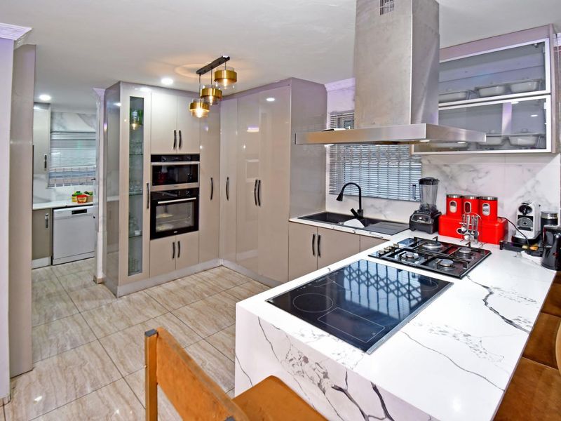 Modern kitchen featuring high-gloss cabinetry, marble-look countertops, dual hobs, built-in appliances, and tiled flooring, with an adjacent scullery area.