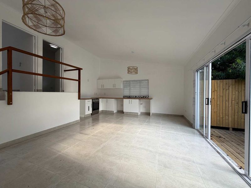 Spacious open-plan living and kitchen area featuring tiled floors, built-in cabinetry, and large sliding doors opening onto a private timber deck.