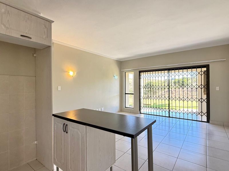 Open-plan living and kitchen area featuring tiled flooring, neutral walls, and a sliding glass door with security gate leading to the exterior.