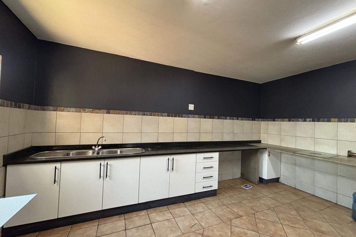A functional kitchen area featuring white cabinetry, dark granite countertops, a double sink, and tiled flooring, suitable for industrial or commercial use.