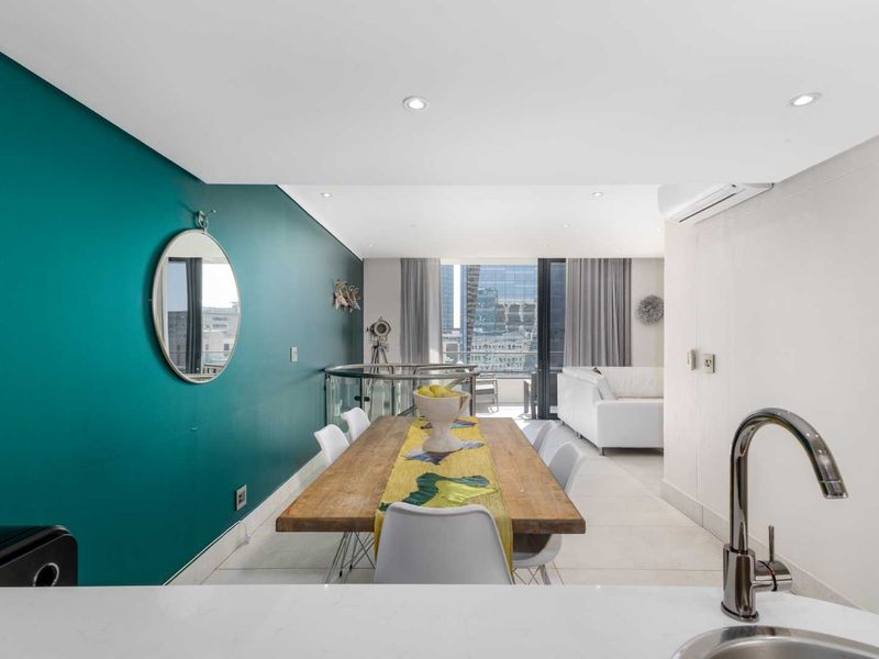 Modern open-plan living and dining area featuring tiled floors, recessed lighting, and a sleek kitchen corner with stone countertops and city views.