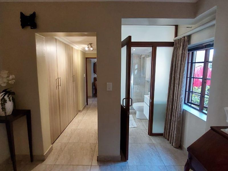 Bedroom featuring tiled flooring, extensive built-in cupboards, and direct access to an en-suite bathroom with a window providing natural light.