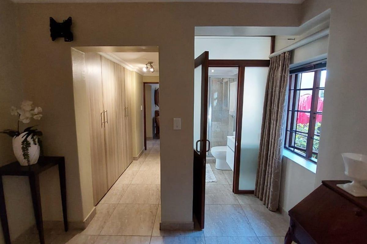 Bedroom featuring tiled flooring, extensive built-in cupboards, and direct access to an en-suite bathroom with a window providing natural light.