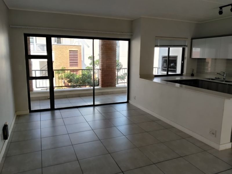 Open plan living area featuring tiled floors, a breakfast bar, and a sliding glass door leading to a private balcony.