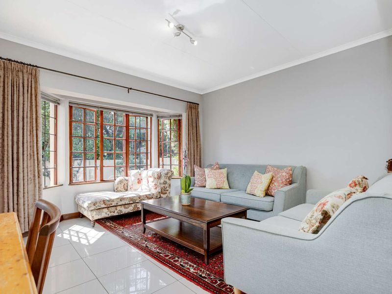A bright living room featuring large bay windows, polished tiled flooring, and neutral wall finishes, offering a comfortable and well-lit space.