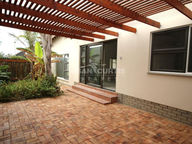 A covered outdoor patio area featuring a timber pergola, brick paving, and sliding door access to the interior living space.