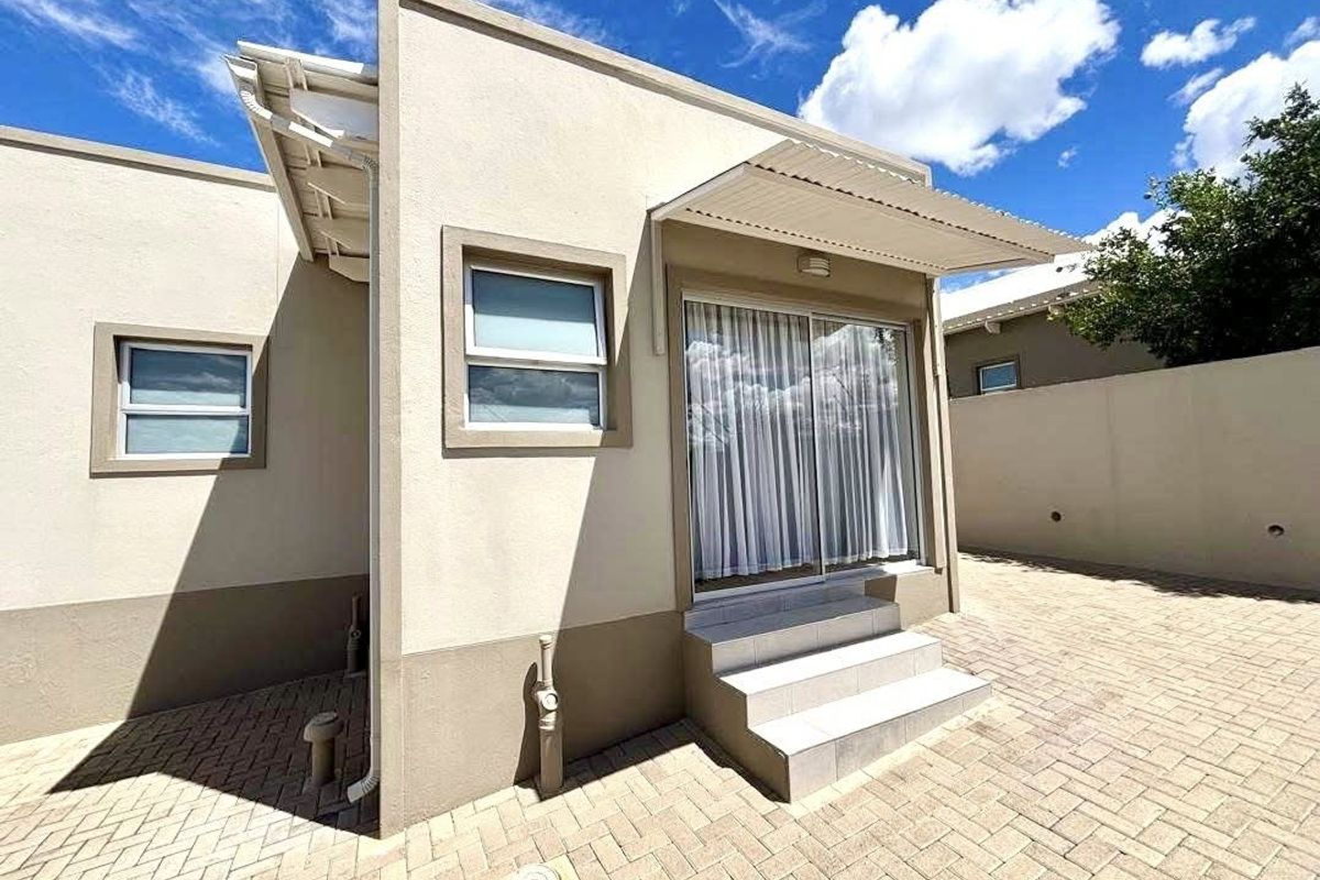 A well-maintained rear exterior view featuring a paved courtyard, sliding glass door access, and a protective metal awning over the entrance steps.