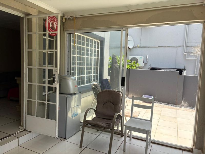 A covered patio area featuring tiled flooring and sliding glass doors, showing signs of unfinished wall plastering and maintenance requirements.