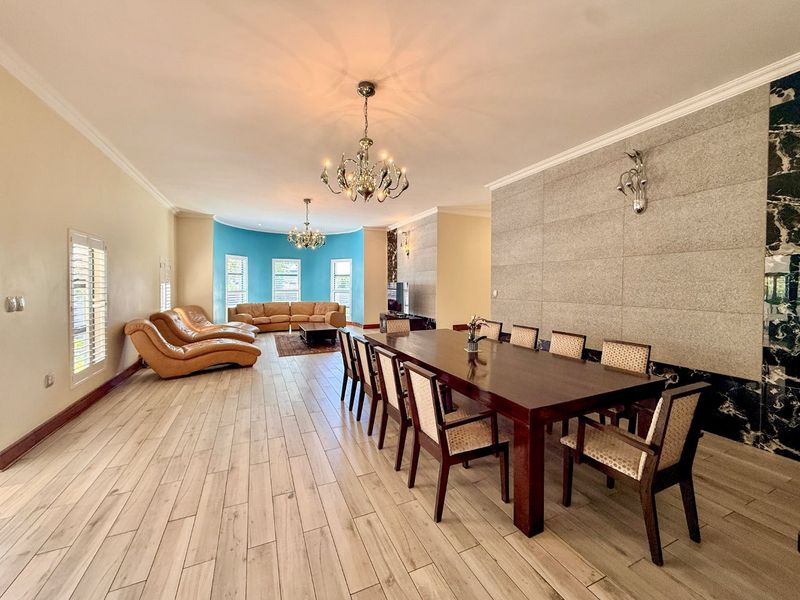 Spacious open-plan living and dining area featuring wood-look tile flooring, a striking stone feature wall, and elegant chandeliers.