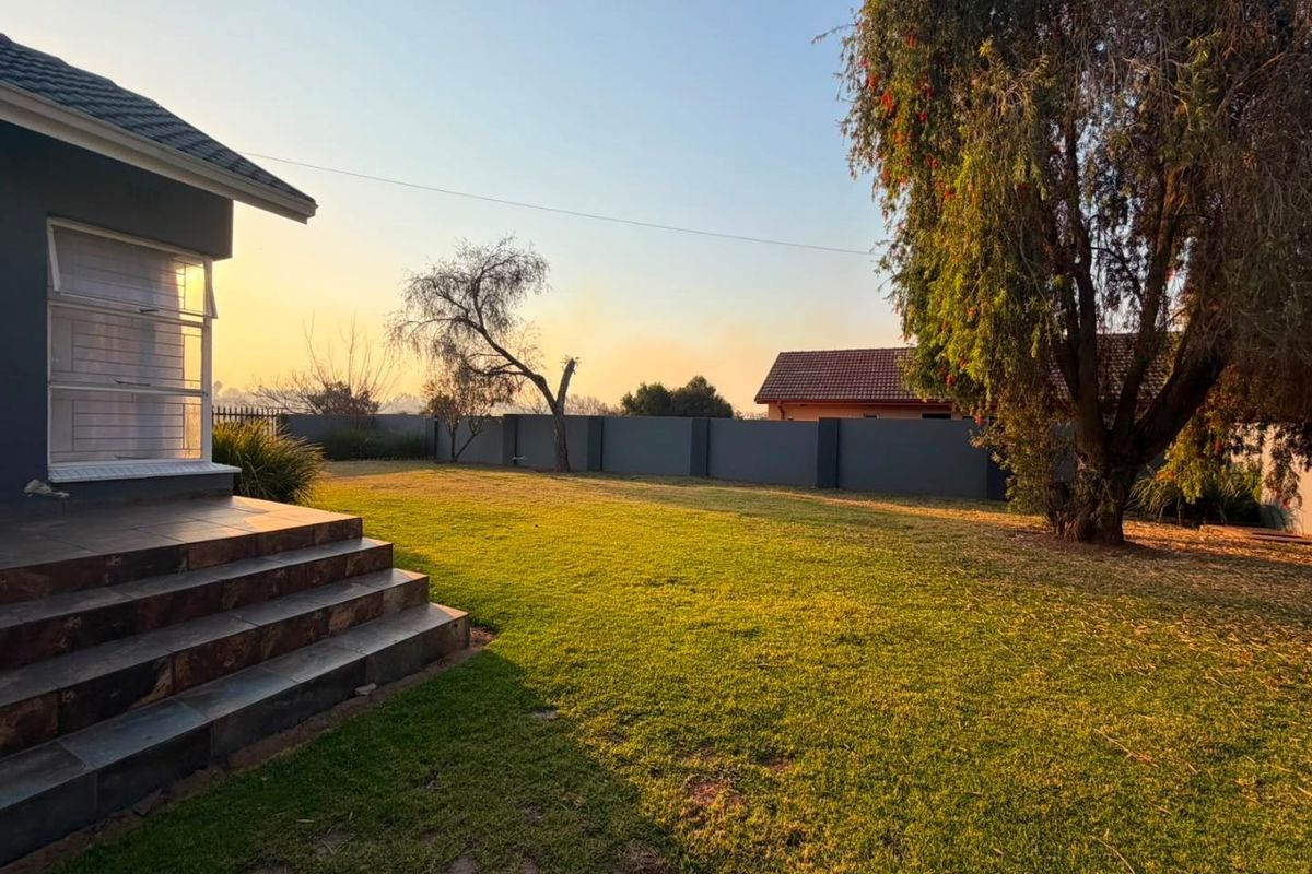 A spacious rear garden featuring a well-maintained lawn, perimeter boundary wall, and tiled steps leading to the house exterior.