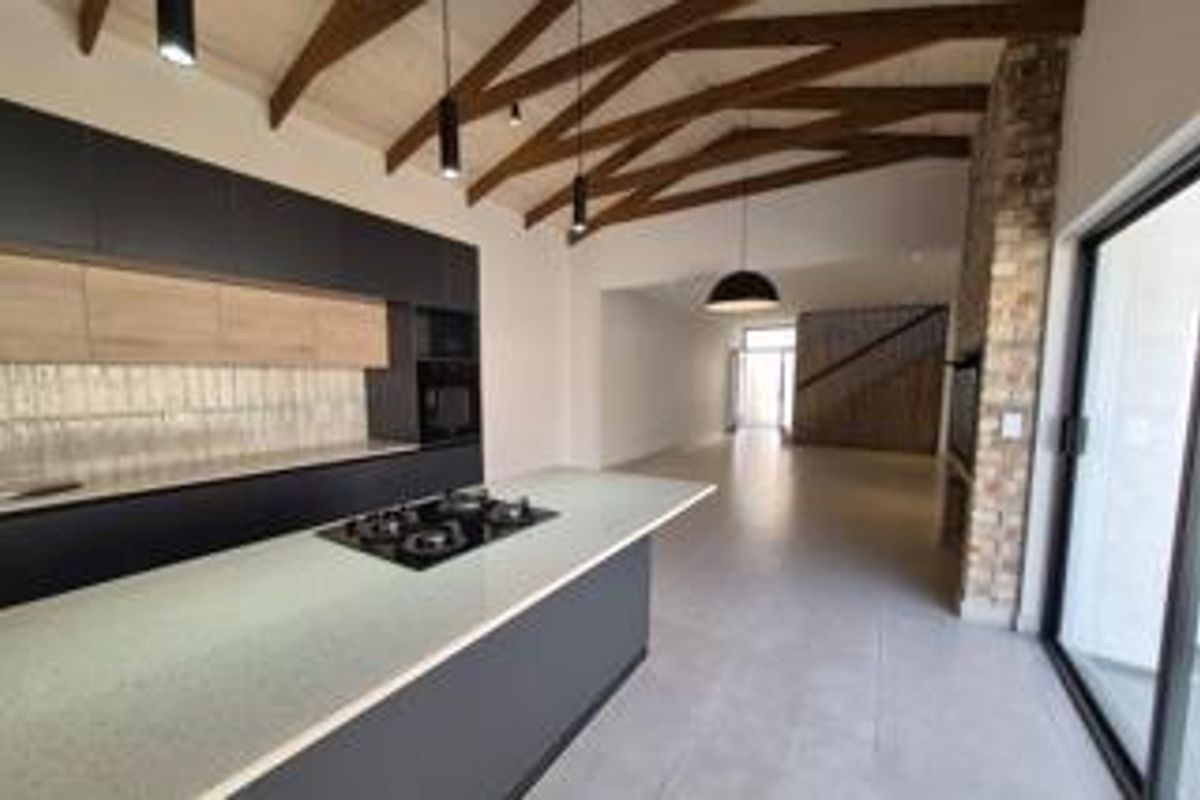 Modern open-plan living area featuring a sleek kitchen with island, gas hob, exposed timber beams, and large sliding doors leading to the exterior.
