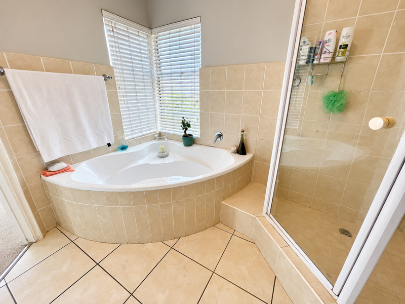 A functional bathroom featuring a corner bathtub, a separate shower enclosure, and neutral ceramic tiling throughout.