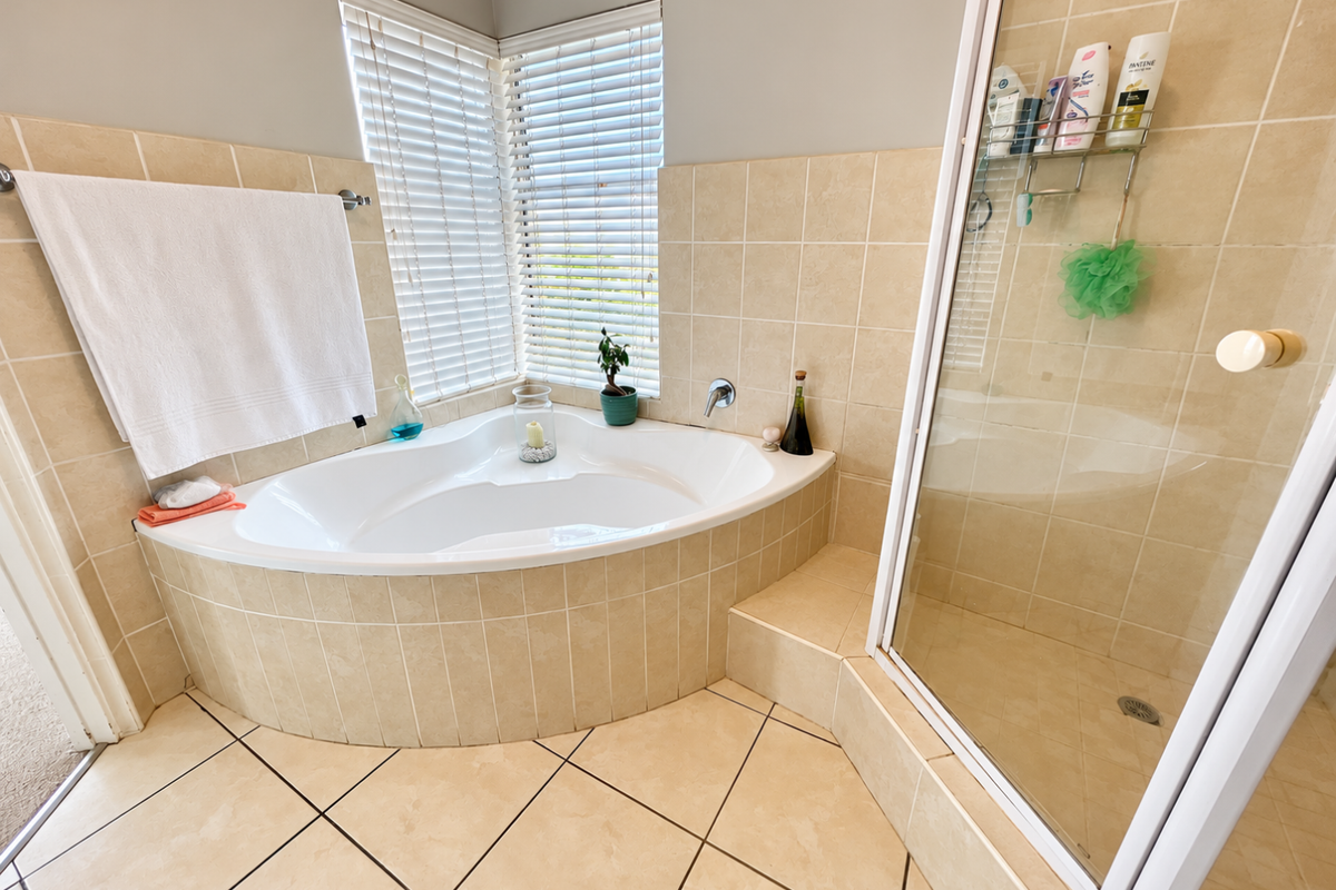 A functional bathroom featuring a corner bathtub, a separate shower enclosure, and neutral ceramic tiling throughout.