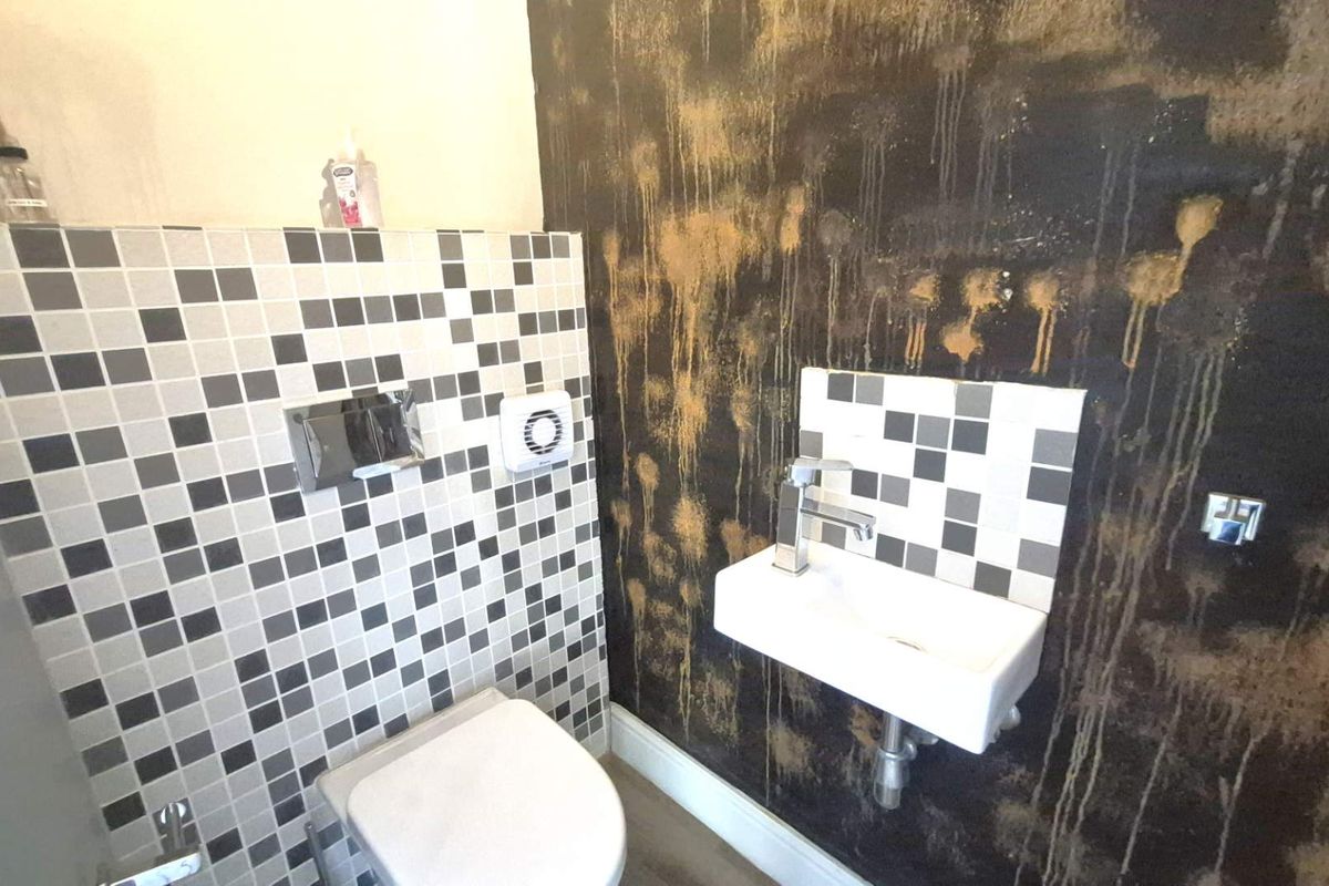 Compact guest bathroom featuring a wall-mounted toilet with concealed cistern, wall-mounted basin, and distinctive decorative wall finish.