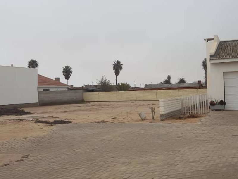 Front view of the property featuring a double garage, paved driveway, and a large, unlandscaped yard area enclosed by boundary walls.