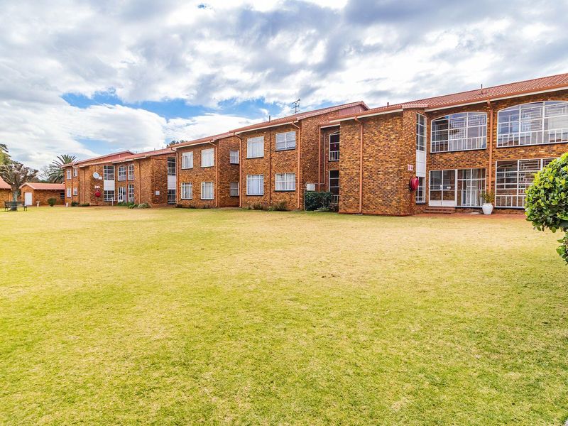 A wide-angle view of the rear facade of a face-brick townhouse complex featuring a large, well-maintained communal lawn area.