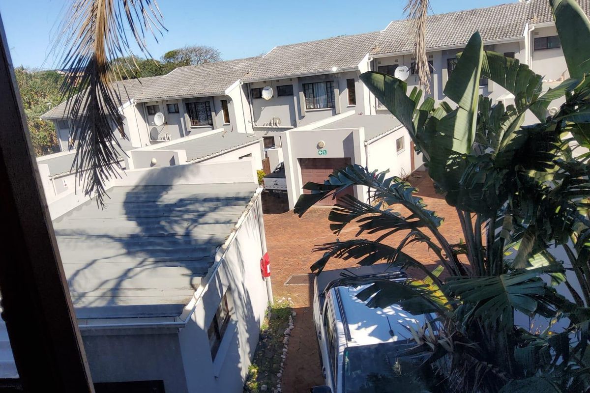 An elevated view of the townhouse complex rear exterior, featuring paved driveways, garage access, and tiled roofing.