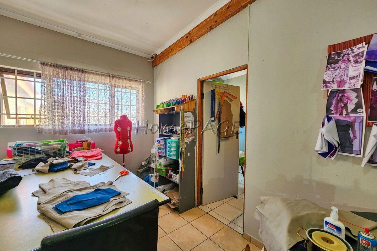 A functional room currently used as a workspace, featuring tiled flooring, timber cornice detailing, and security bars on the window.