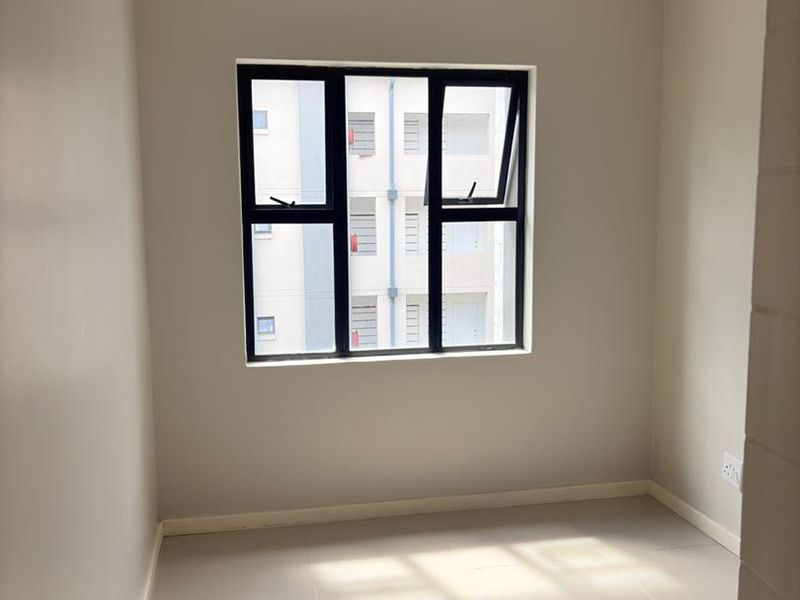 A bright, empty bedroom featuring neutral walls, tiled flooring, and a modern black-framed aluminium window.