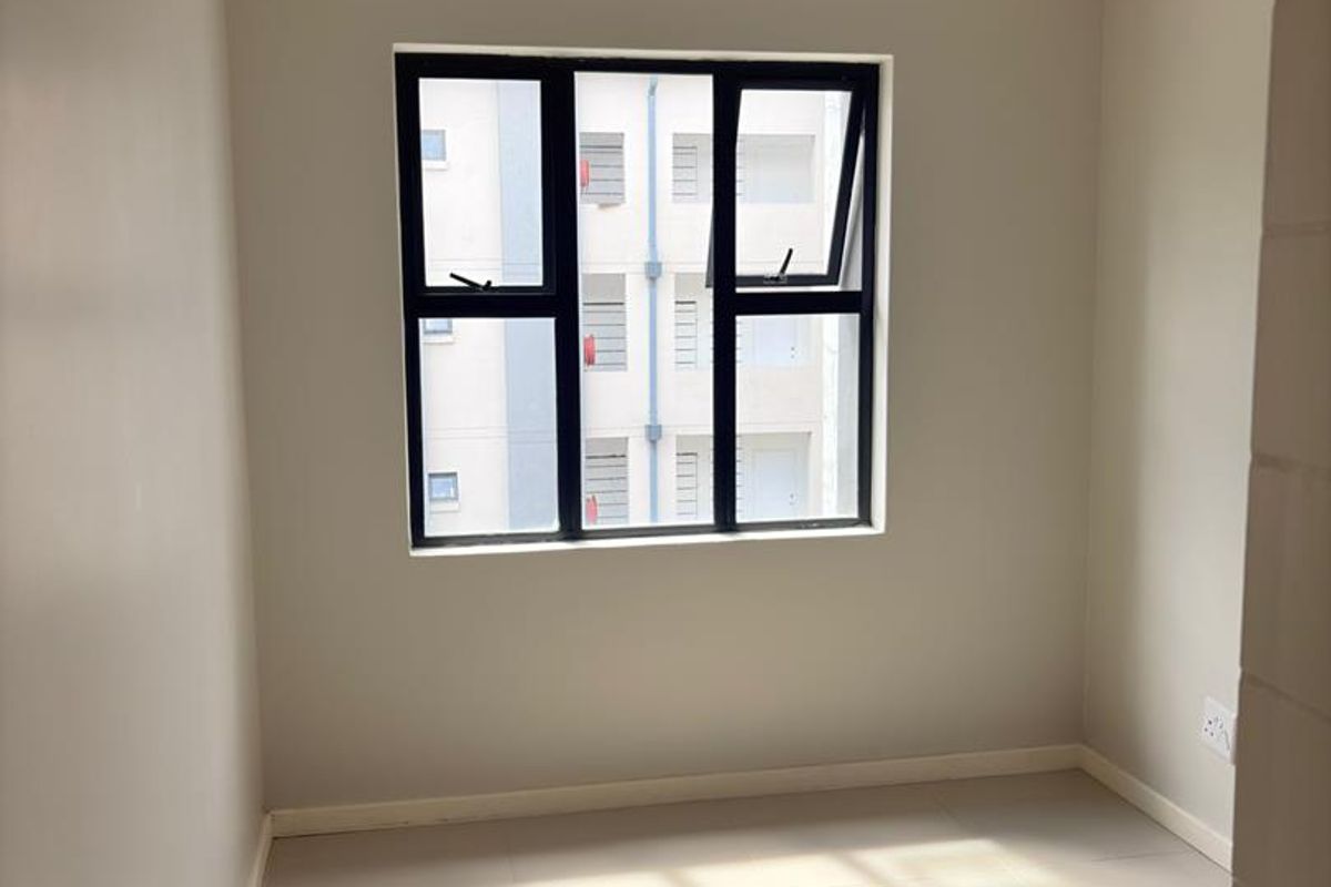 A bright, empty bedroom featuring neutral walls, tiled flooring, and a modern black-framed aluminium window.