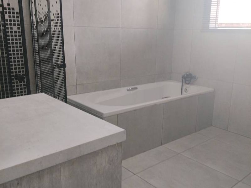 A modern bathroom featuring a built-in bathtub, tiled finishes, and a glass shower screen, presenting a clean and neutral aesthetic.