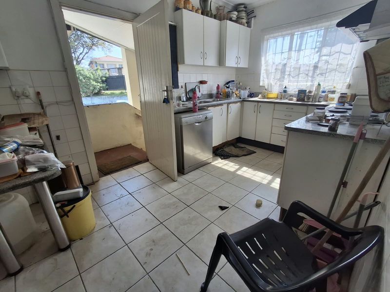 A functional kitchen featuring built-in cabinetry, tiled flooring, and a tiled backsplash, with direct access to an exterior entrance.
