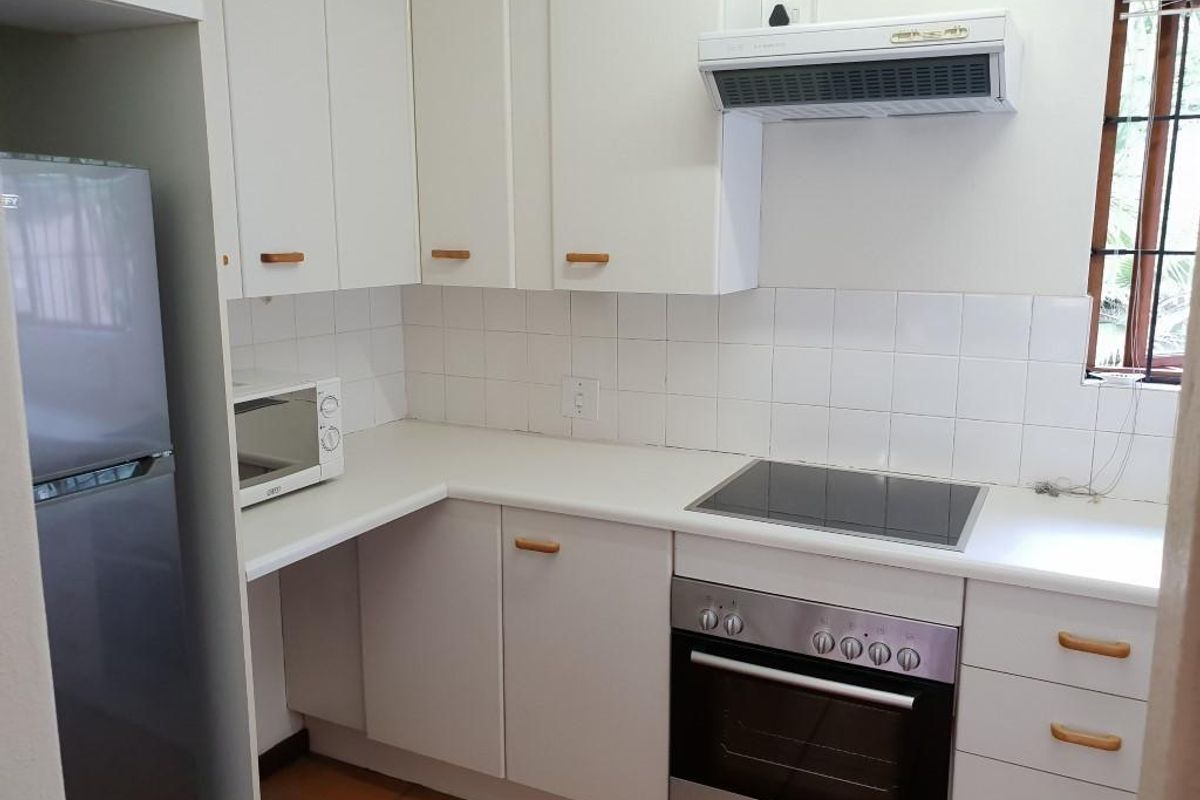 Compact kitchen featuring white cabinetry, tiled splashback, built-in oven, electric hob, and extractor fan.