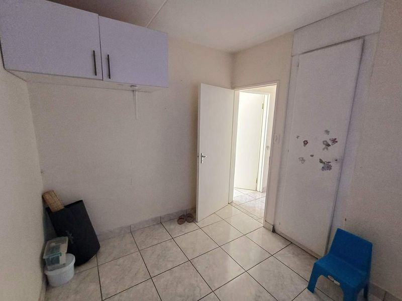 A compact bedroom featuring tiled flooring, a built-in cupboard, and overhead storage cabinetry, presenting a blank canvas for potential interior updates.