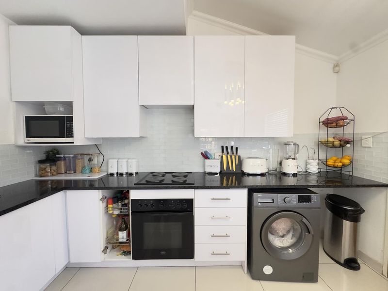 Modern kitchen featuring white high-gloss cabinetry, black granite countertops, subway tile backsplash, and integrated appliances including an oven, hob, and microwave.