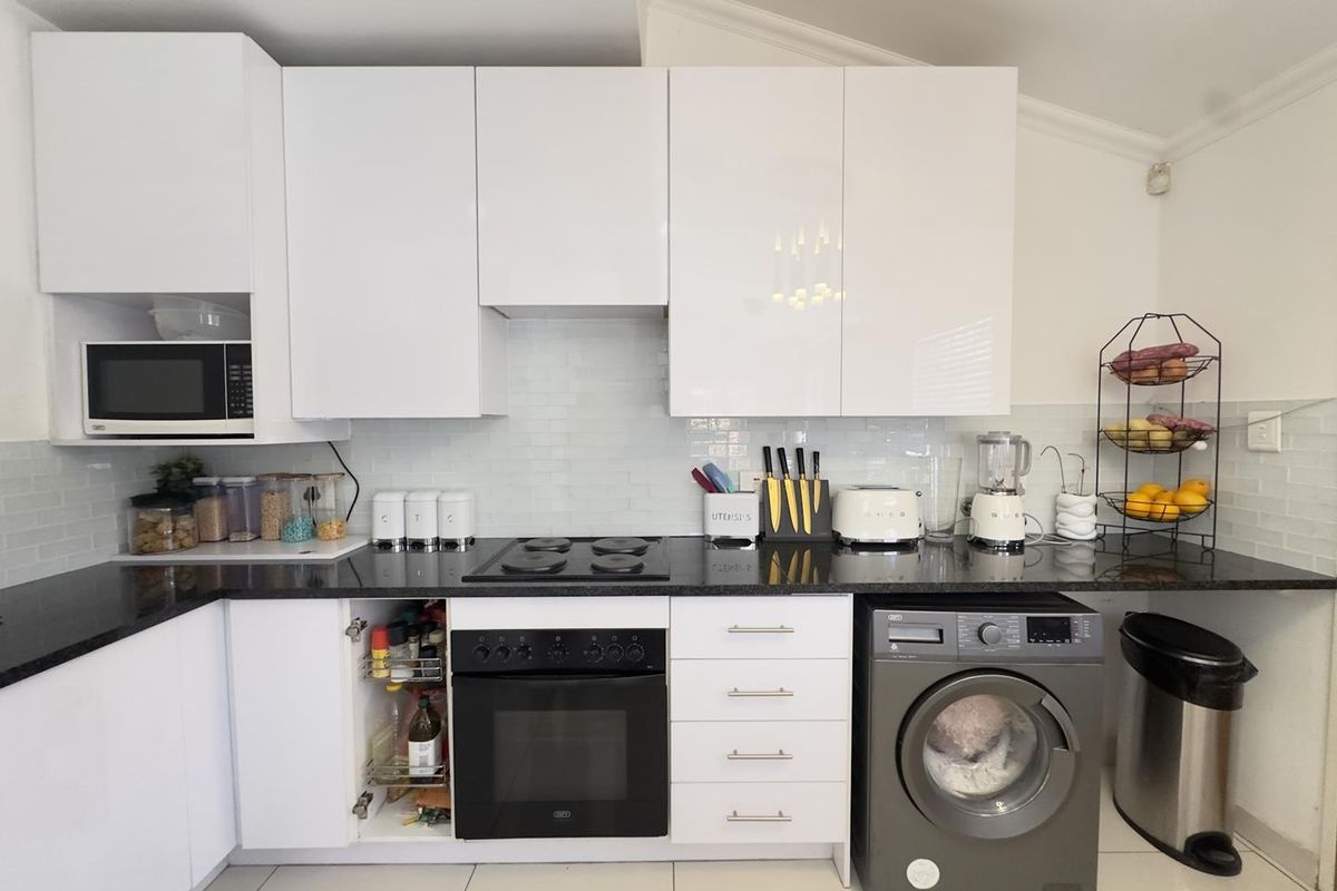 Modern kitchen featuring white high-gloss cabinetry, black granite countertops, subway tile backsplash, and integrated appliances including an oven, hob, and microwave.
