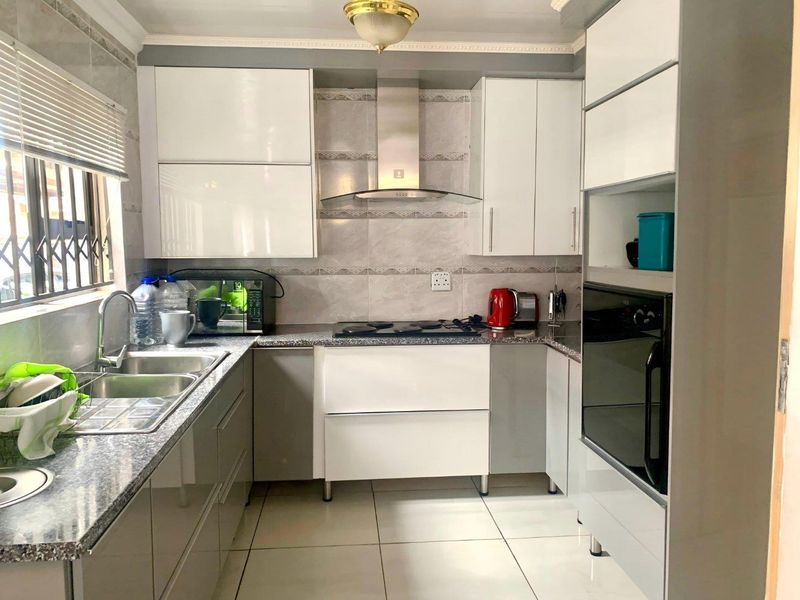 A modern, well-maintained kitchen featuring high-gloss cabinetry, granite countertops, a built-in oven, hob, and extractor fan with tiled finishes throughout.