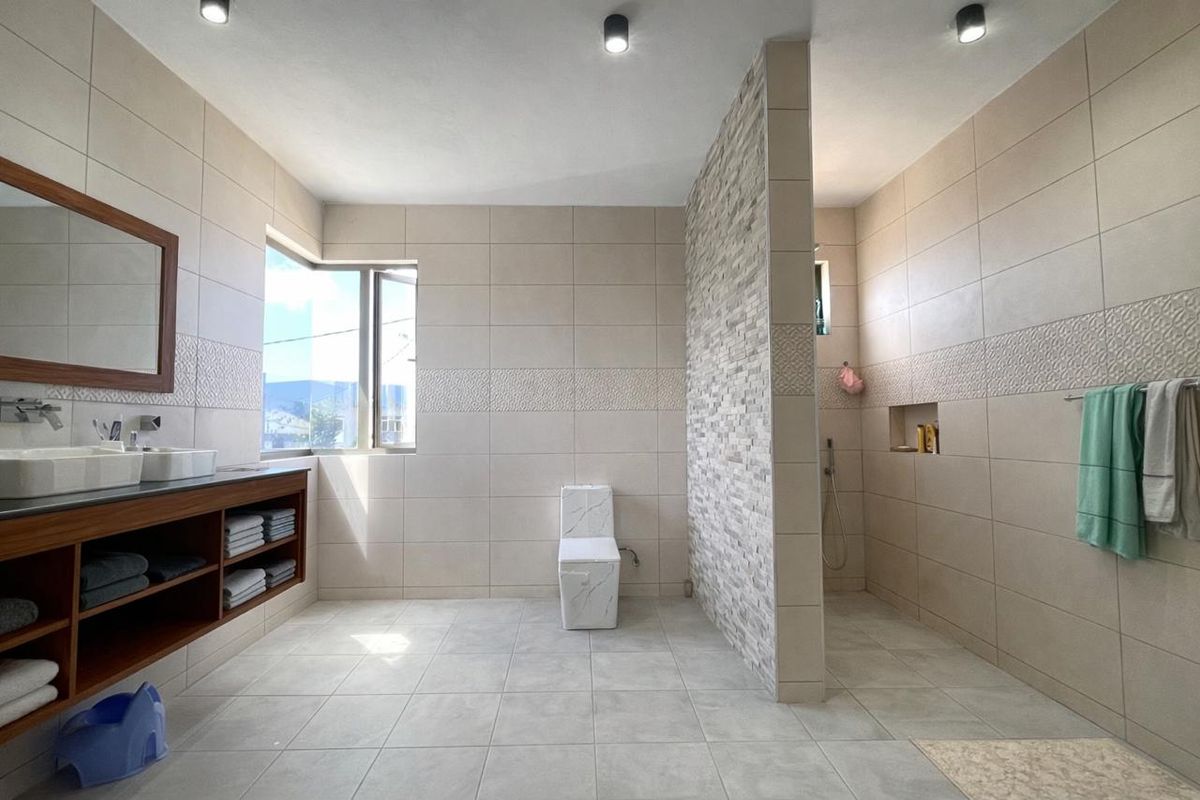 Modern bathroom featuring a double vanity with wooden cabinetry, a walk-in shower with stone-cladding feature wall, and a contemporary toilet.