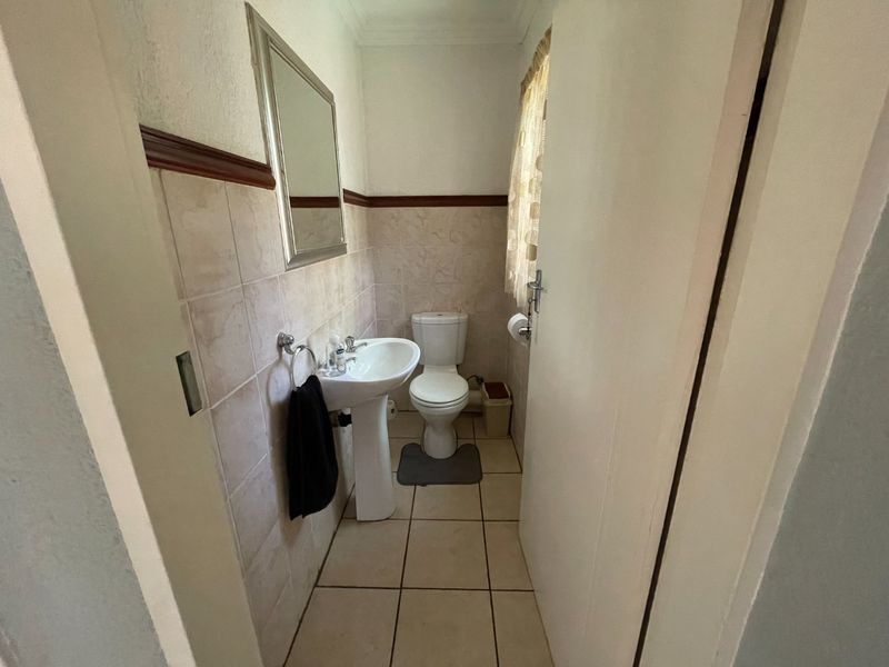 A compact guest bathroom featuring a pedestal washbasin, toilet, and neutral wall and floor tiling.