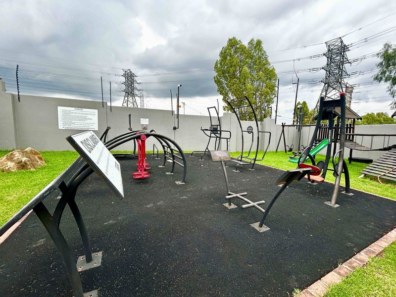 Outdoor fitness area featuring various exercise stations, rubberized safety flooring, and a secure perimeter wall with electric fencing.
