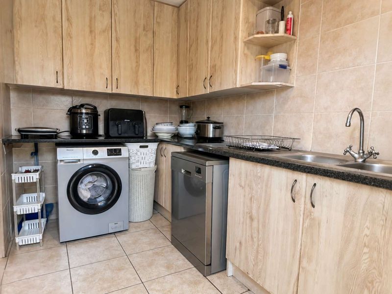 A functional scullery featuring light wood-look cabinetry, granite countertops, a stainless steel sink, and tiled finishes throughout.